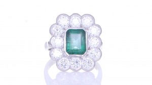 Green Emerald Surrounded By Twelve Diamonds Placed On A Silver Ring