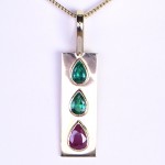 Two Green Emeralds And A Ruby Placed On A Gold Pendant