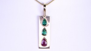 Two Green Emeralds And A Ruby Placed On A Gold Pendant
